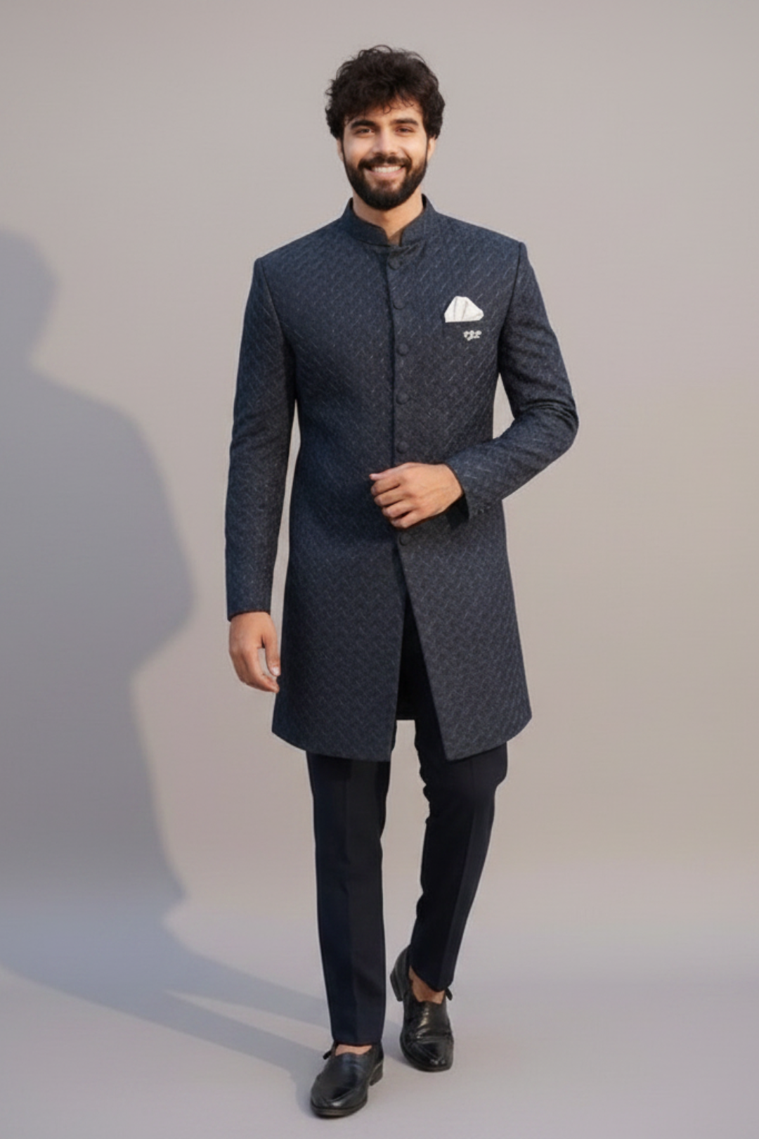 Man wearing a dark blue traditional outfit with a white pocket square on a gray background