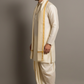 Man wearing a traditional cream sherwani with gold accents on a gray background