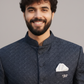 Man wearing a dark blue traditional jacket with a white pocket square against a gray background