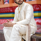 Man in traditional white sherwani sitting on a bench with colorful background