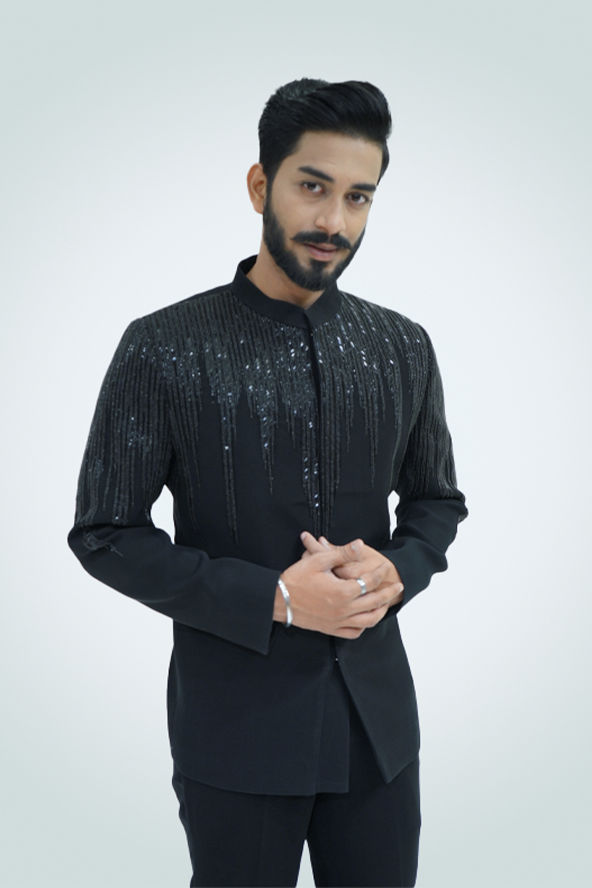 A man wearing a black shirt with wood crepe fabric and embellishments, paired with black trousers.