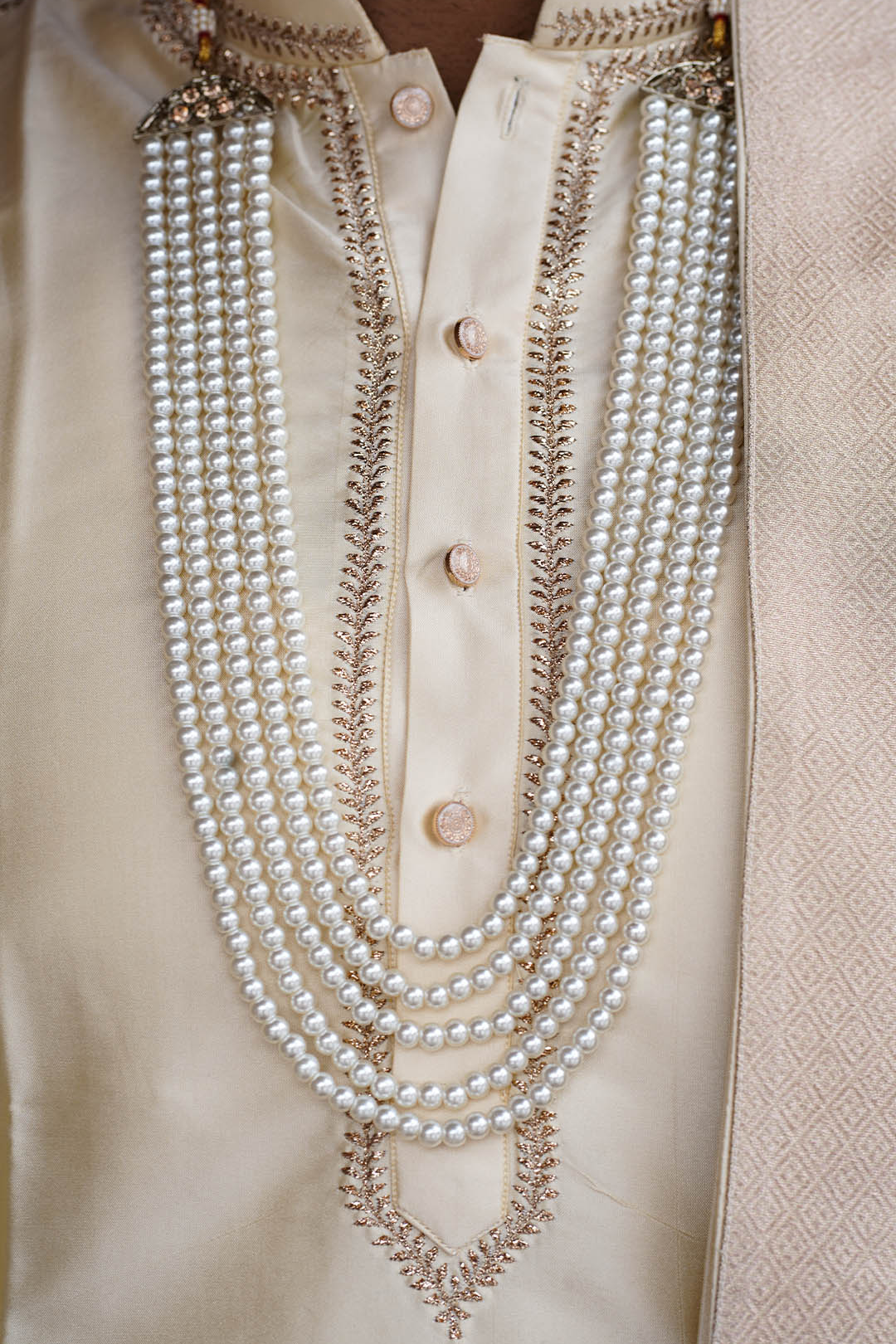 Close-up of a pearl necklace draped over a beige garment with buttons.