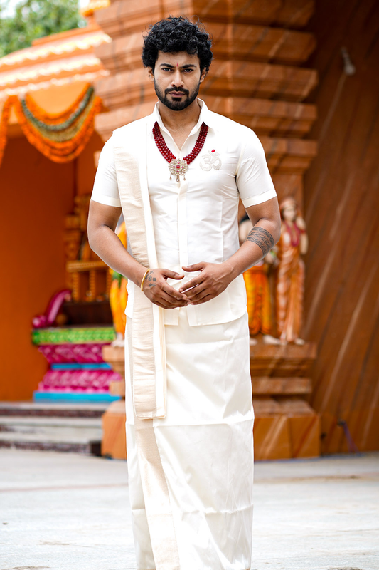 Man in traditional white attire standing in front of a temple structure