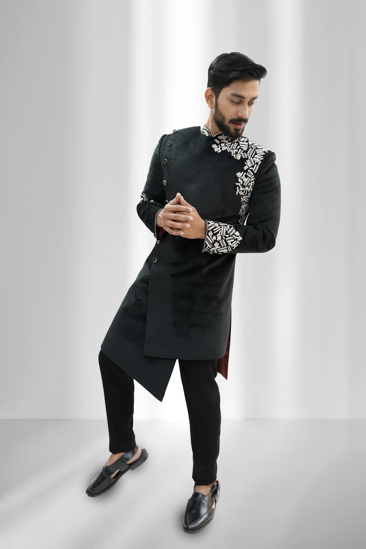 A man wearing a black asymmetrical Indo-Western sherwani with silver zardozi work on the sleeves and chest.