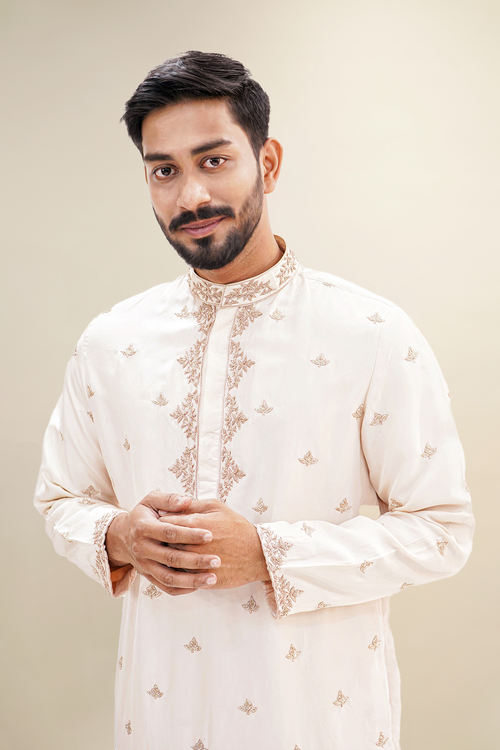 A man wearing a rose pink habutai kurta with zardozi butta work, standing with a smile.