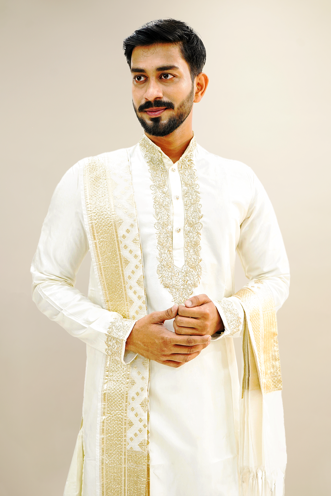 A man wearing an off-white semi-pattu kurta set with zari embroidery, standing against a light background.