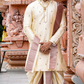 Man in traditional cream and maroon outfit standing in front of ornate pink architectural background