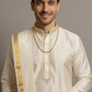 Man wearing a traditional cream kurta with gold embroidery and border against a gray background