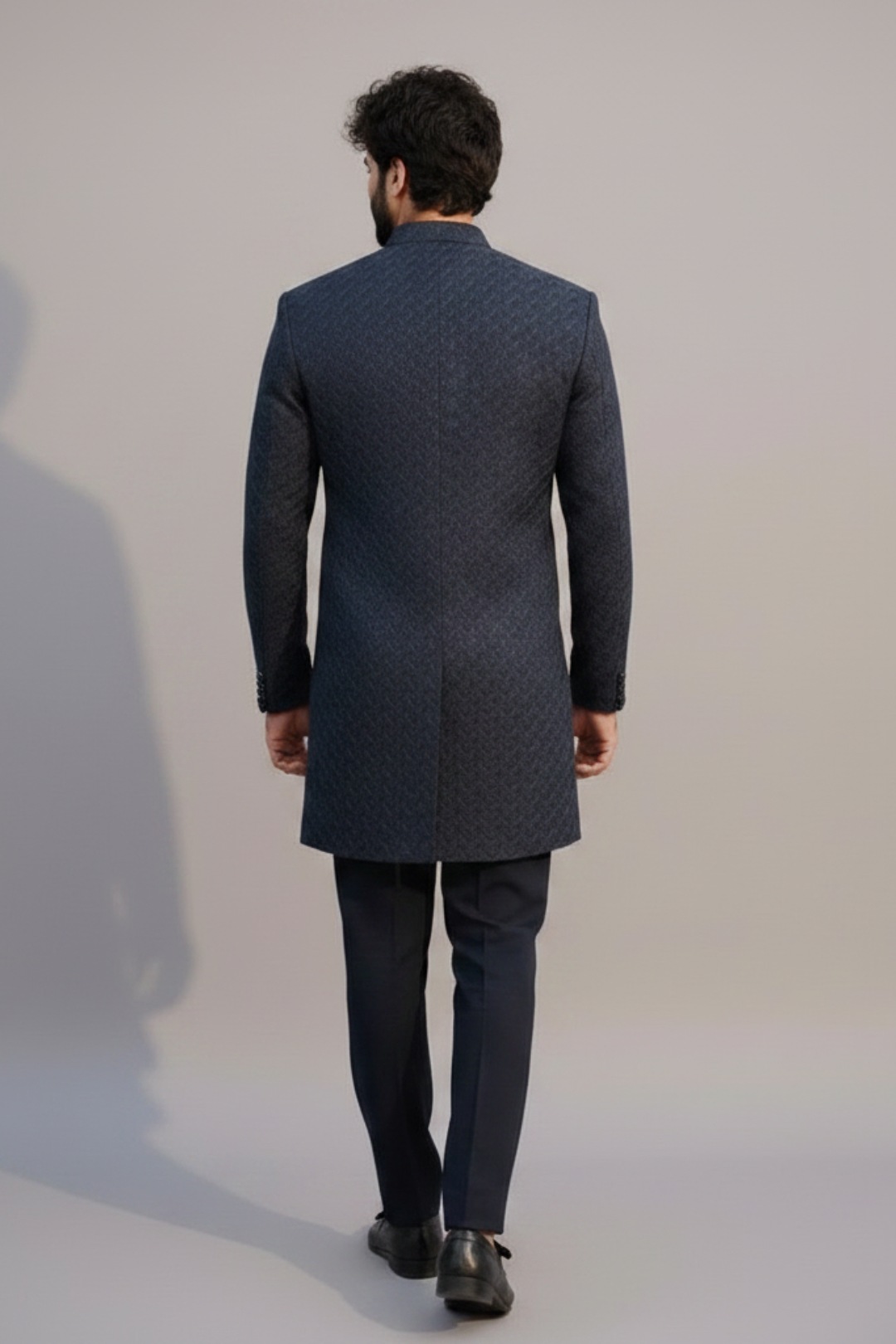 Man wearing a dark blue patterned coat and pants on a plain background
