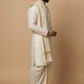 Man wearing a traditional white and gold kurta with dhoti on a beige background