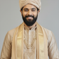 Man wearing a traditional beige outfit with a turban on a gray background