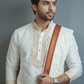 Man wearing a traditional white kurta with red and gold accents against a gray background