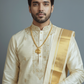Man wearing a traditional cream sherwani with gold embroidery on a gray background
