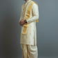Man wearing a traditional cream and gold kurta with dhoti on a gray background