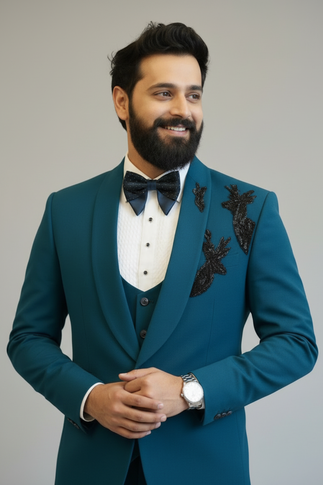 Man wearing a teal suit with black bow tie and floral embroidery on a gray background