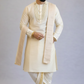 Man wearing a cream sherwani with a white dhoti on a gray background