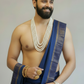 Man wearing a blue saree with gold jewelry on a plain background