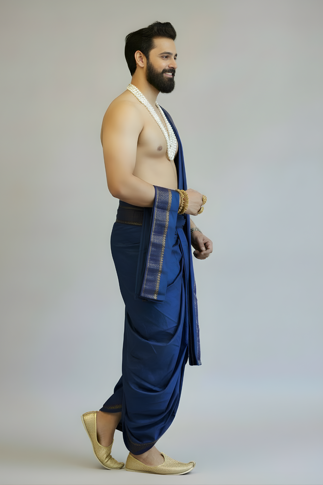 Man wearing a blue dhoti with a white cloth over his shoulder against a plain background