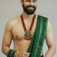 Man wearing a green traditional outfit with gold jewelry on a plain background