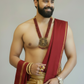 Man wearing a red and gold traditional outfit with jewelry on a plain background