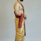 Man wearing a traditional gold dhoti with a red border on a plain background