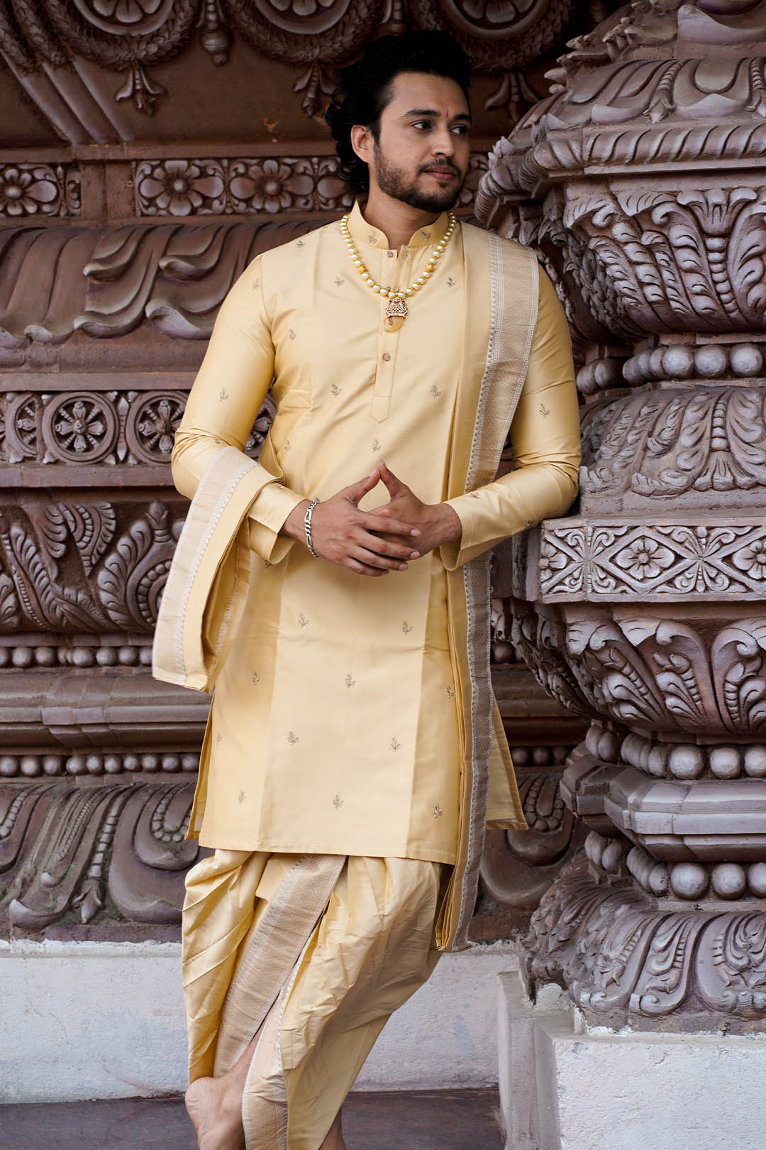 Man in a traditional yellow kurta standing in front of ornate stone architecture.