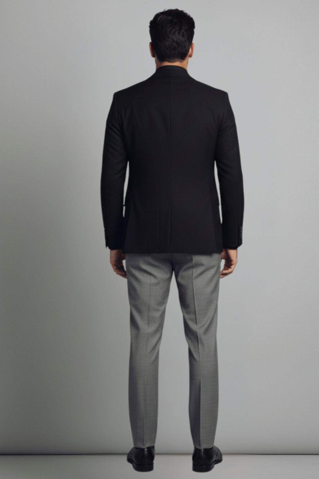 Man wearing a black blazer and gray pants against a plain background