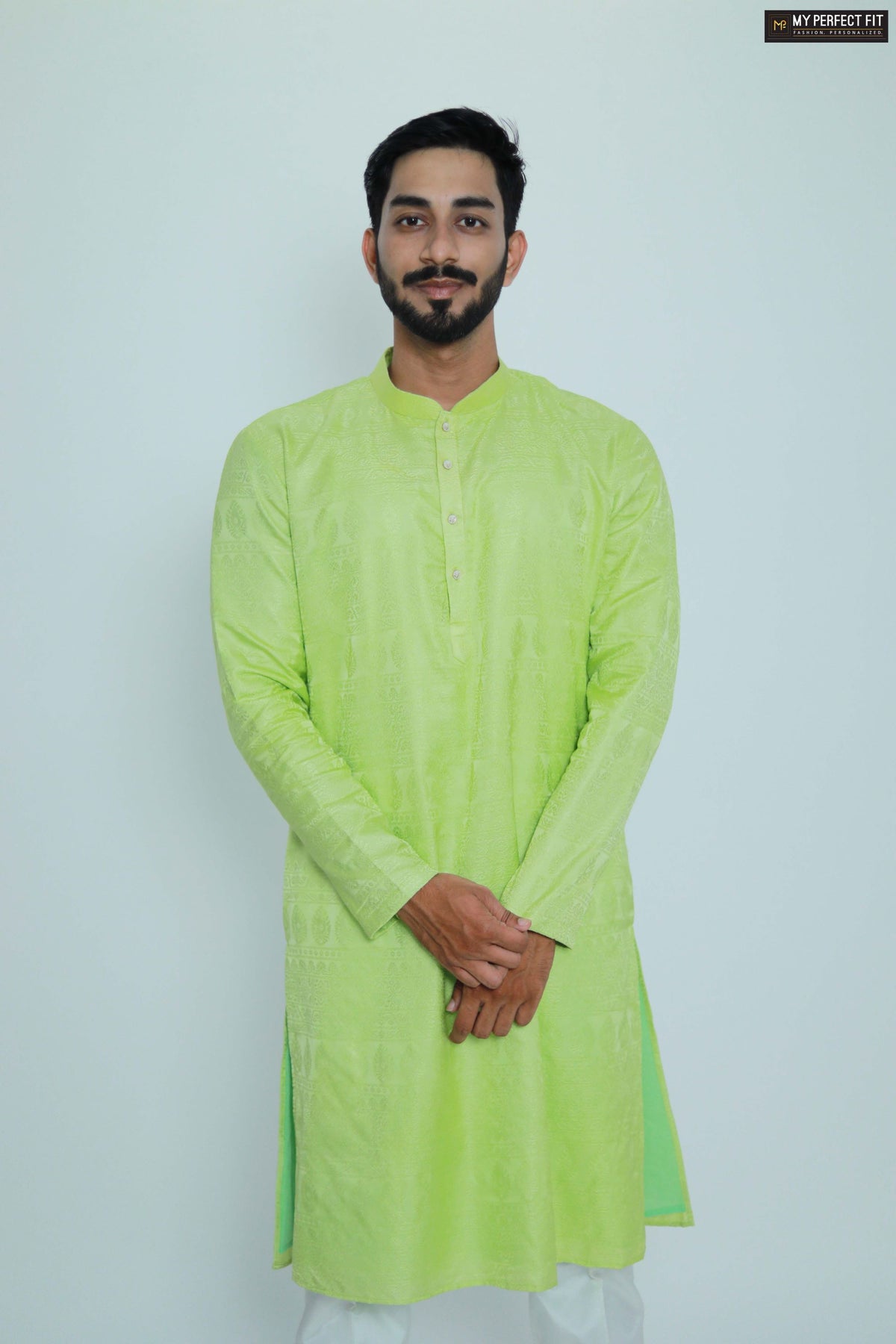A person standing against a white background, wearing a green jacquard kurta with full-length sleeves, paired with white trousers.
