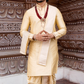Man in traditional cream kurta with maroon border standing against an ornate brown wall.