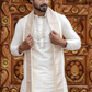 Man wearing a traditional white kurta with a cream shawl against an ornate wooden background