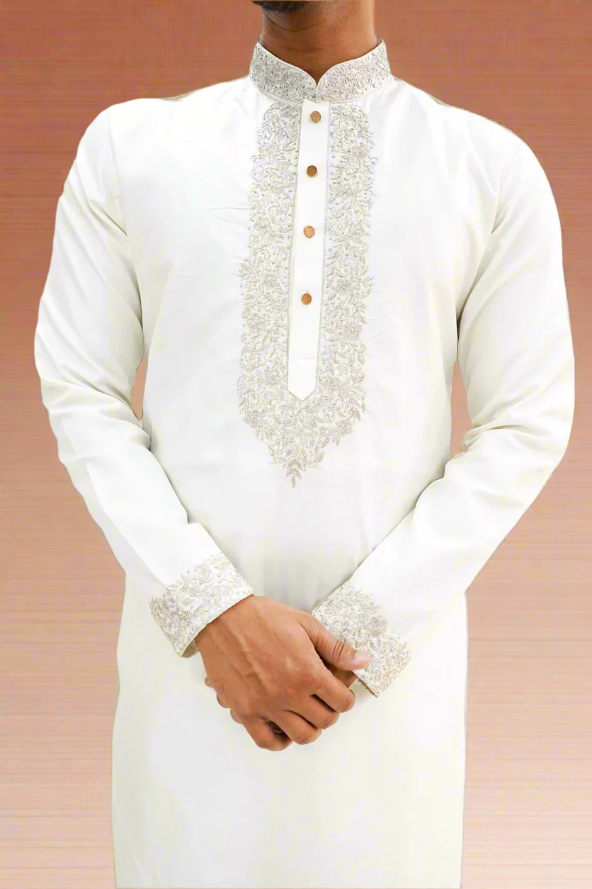 A man wearing an off-white semi-pattu kurta with zari embroidery, standing against a beige background.
