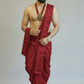 Man wearing a red dhoti with gold jewelry on a plain background