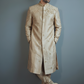 Man wearing a beige sherwani against a gray background