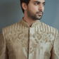 Man wearing a beige embroidered traditional outfit against a gray background