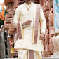 Man in traditional cream and maroon outfit standing in front of a temple.