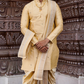 Man wearing a traditional yellow kurta with white dhoti in front of an ornate wall.