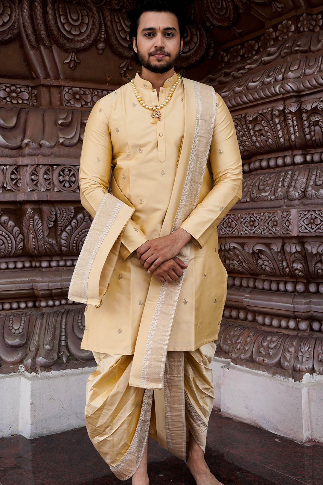 Man wearing a traditional yellow kurta with white dhoti in front of an ornate wall.