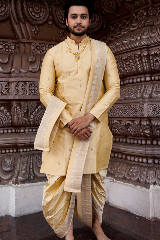 Man wearing a traditional yellow kurta with white dhoti in front of an ornate wall.
