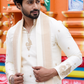 Man wearing a traditional white sherwani with intricate designs against a colorful background