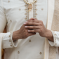 Person wearing a traditional embroidered outfit with a focus on hands and jewelry.