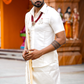 Man in traditional white outfit holding a staff in front of an orange backdrop with statues.