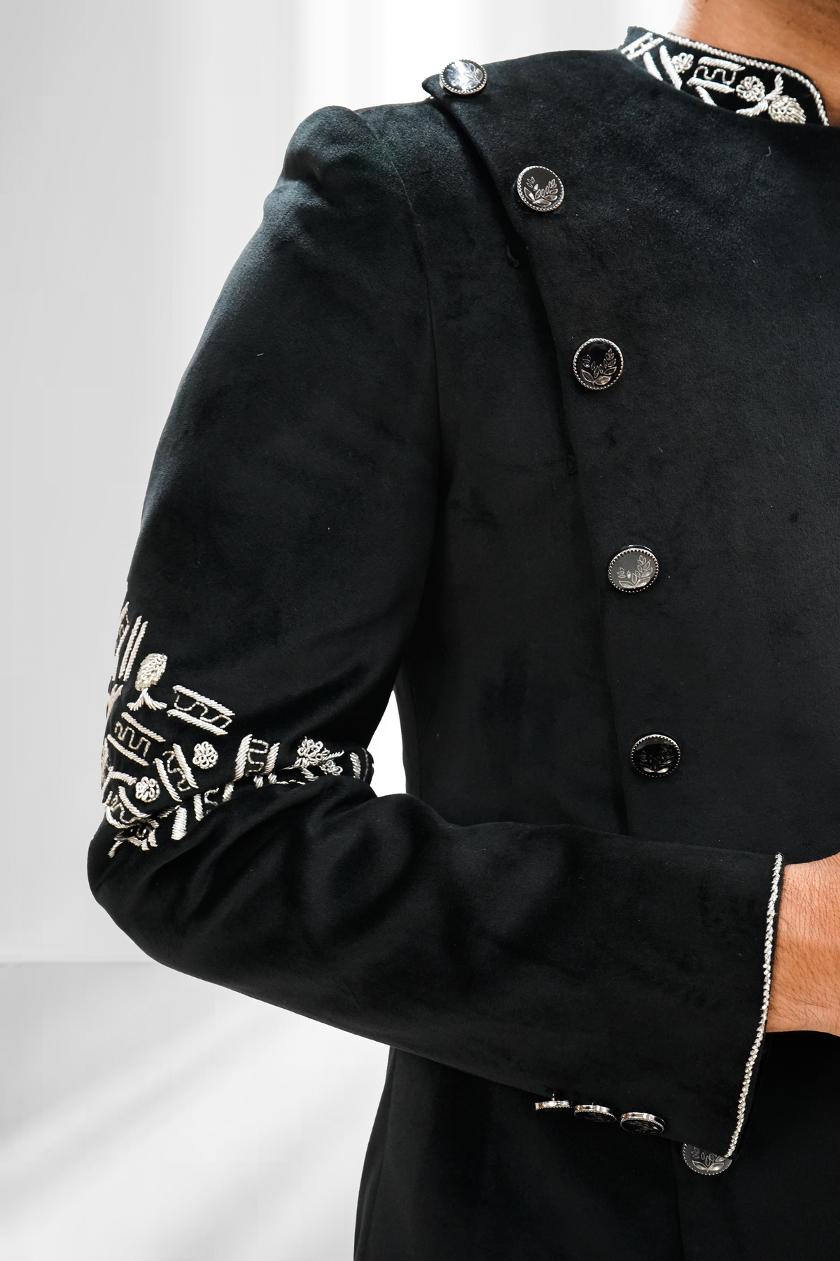 A man wearing a black asymmetrical Indo-Western sherwani with silver zardozi work on the sleeves and chest.