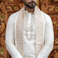 Man wearing a traditional white sherwani with intricate embroidery against a decorative wooden background