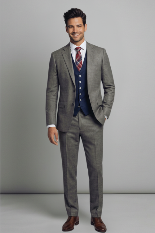 Man wearing a gray suit with a blue vest and red tie against a plain background