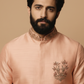 Man wearing a peach embroidered kurta against a beige background