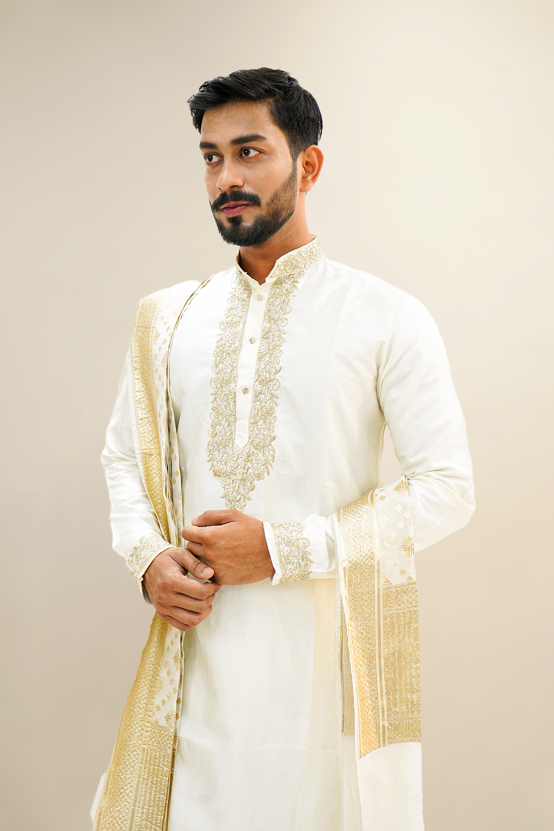 A man wearing an off-white semi-pattu kurta set with zari embroidery, standing against a light background.