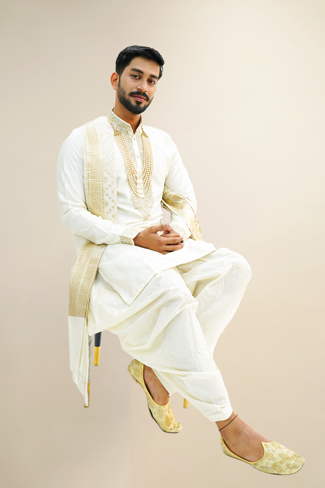 A man wearing an off-white semi-pattu kurta set with zari embroidery, standing against a light background.