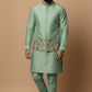 Man wearing a traditional green kurta with floral embroidery on a beige background