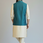 Man wearing a teal vest over a cream kurta with white pants on a plain background