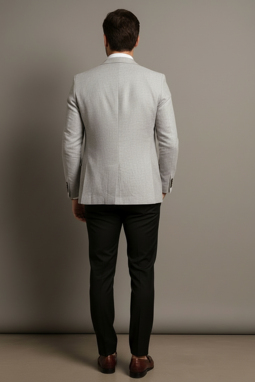 Man wearing a light gray checkered blazer and black pants against a plain background